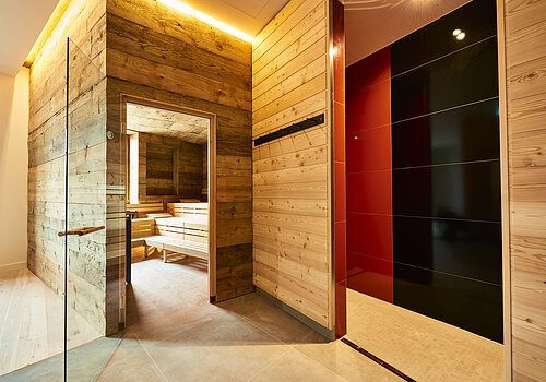 Die Glastür der Sauna aus Holz steht offen und wir können einen Blick auf die leeren Bänke darin werfen.