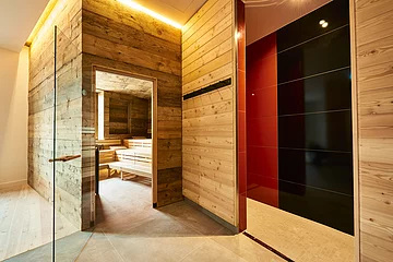 Die Glastür der Sauna aus Holz steht offen und wir können einen Blick auf die leeren Bänke darin werfen.