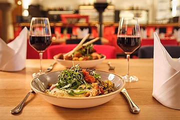 Tisch mit zwei Tellern, zwei Gläsern Rotwein, Besteck und zwei gefalteten weißen Servietten in einem Restaurant.