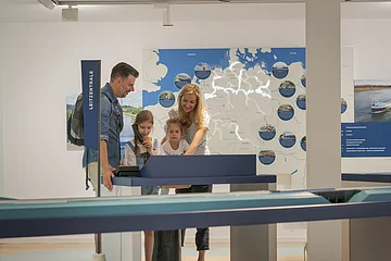 Familie mit zwei Kindern steht an interaktivem Ausstellungstisch vor beleuchteter Deutschlandkarte im Museum.