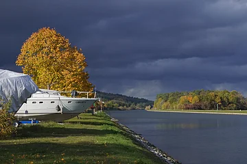 Boot mit dem Namen Liberty am Ufer eines Flusses, herbstliche Bäume und dunkler Himmel im Hintergrund.